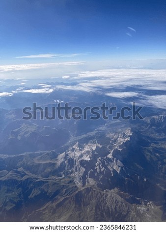 View from flying airplane in the sky in sunny blue sky with clouds. City, fields and forest landscape from airplane window view. Cityscape and nature landscape from the sky. Houses and trees view. 
