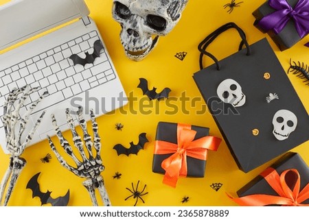 Snagging the best Halloween presents via online shopping. Top view shot of laptop, skeleton hands, skull, presents, scary insects on yellow background