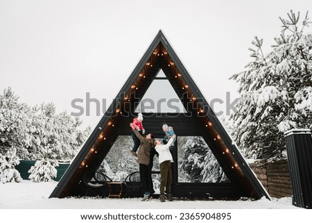 Family with kids have fun on terrace of mountain country house in snow forest. Winter holidays outdoors. Mother, father, daughter, son spend holidays at cottage. Mom, dad with child celebrate New Year