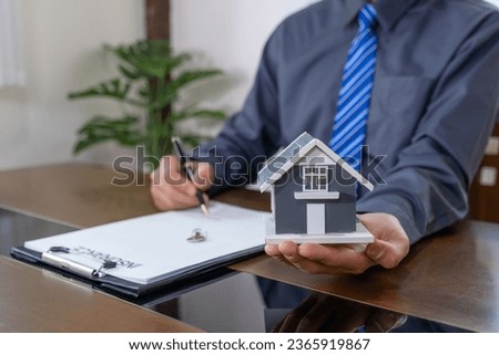 Real estate agents hand holding home model, explains the business contract for signing a business contract, renting, buying, mortgage, loan or home insurance.