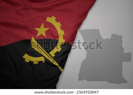 big waving national colorful flag and map of angola on the gray background. macro