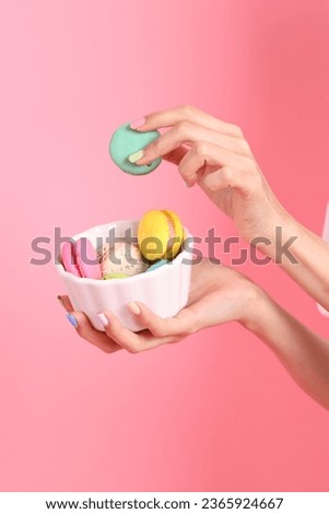 The Asian woman holding macaroons in the hand on the pink background.