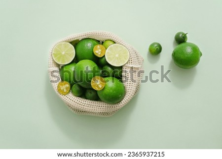 View from above of many kumquat and lime contained inside a mesh bag. Pastel background. Lime and Kumquat juice may promote weight loss