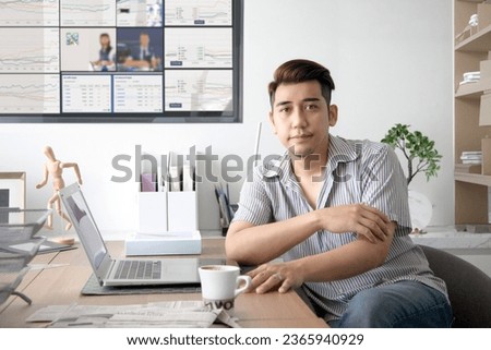Confident asian man trading stock market with laptop on working desk with investing graph and news on TV  