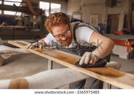 Craftsman coating a wooden board with protective oil in a workshop. Process of making a wood table Royalty-Free Stock Photo #2365975485