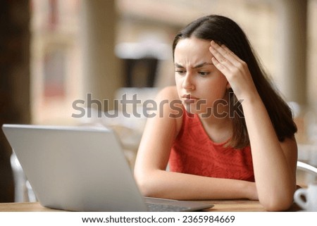 Worried woman checking laptop content sitting in a restaurant terrace Royalty-Free Stock Photo #2365984669