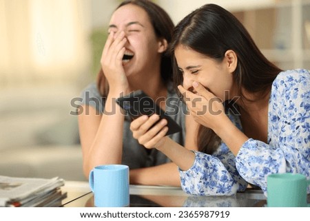 Funny friends watching media on phone laughing loud at home Royalty-Free Stock Photo #2365987919