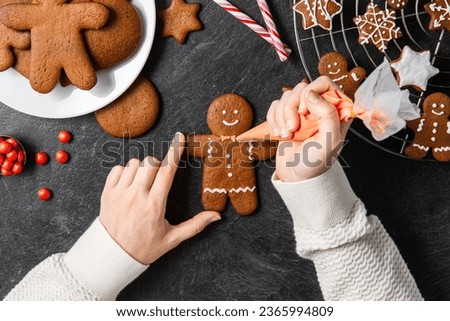 baking, cooking, christmas and food concept - close up of hands with pastry bag decorating gingerbread cookies with white icing on black table top