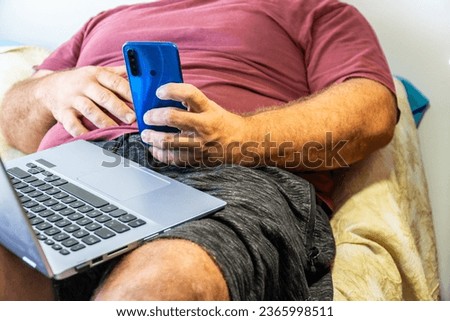 Unrecognizable person. Sedentary overweight man, sitting using a phone Royalty-Free Stock Photo #2365998511