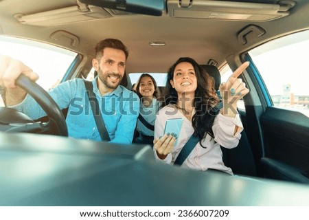 Happy family of three driving automobile, woman using cellphone gps application and showing way to driver man riding new car, view from auto dashboard Royalty-Free Stock Photo #2366007209