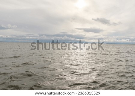 Seascape: waves on the sea on a cloudy day, with the sun breaking through the clouds, shining its rays onto the water