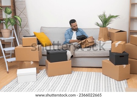 Relishing the joys of relocation and a fresh start, a young man happily unboxes his belongings in his new home, surrounded by cardboard boxes on moving day