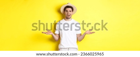 Concept of tourism and summer. Confused guy traveller shrugging, cant understand something, standing against yellow background. Royalty-Free Stock Photo #2366025965