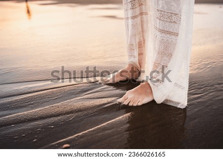 feet of beautiful woman in beautiful white dress on the shore of the beach wet by the waves