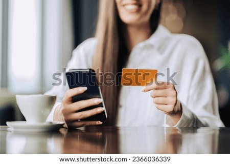 Selective focus on hands holding a credit card and a phone. Close up of a young happy woman using e-banking, online banking, and checking her bank account. Cropped picture of a woman shopping online.