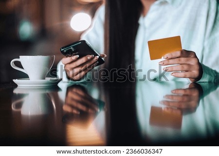 Cropped picture of a woman's hands holding a credit card and a phone for online shopping, e-banking, e-transactions, and booking. Hands holding a credit card and a phone in the cafe.