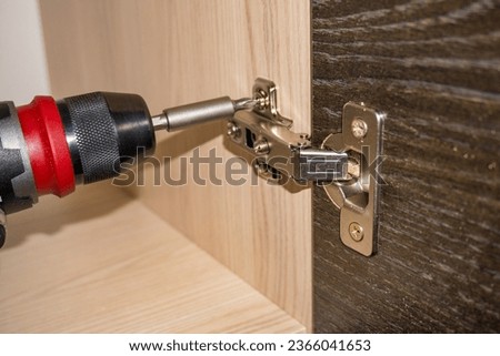 Close-up image of handyman assembling kitchen cabinet and screwing door hinge Royalty-Free Stock Photo #2366041653