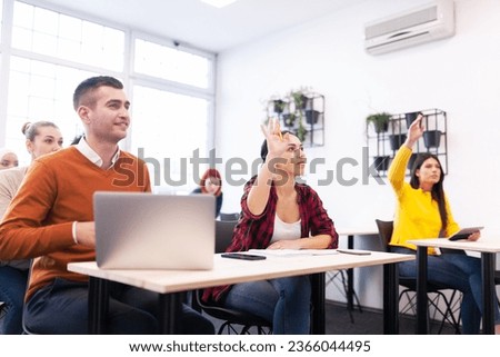 Multi ethnic students listening to a lecturer in a classroom. Smart young people rasing hands during class. Royalty-Free Stock Photo #2366044495