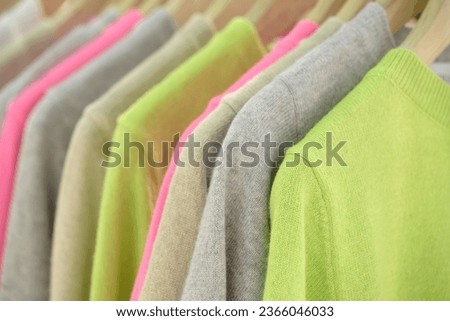Different colorful woolen knitted sweatshirts on the shoulders in the retail clothing store. Selective focus.