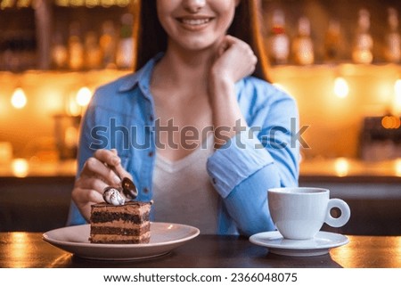 Cropped image of beautiful girl eating cake and smiling while sitting at the cafe