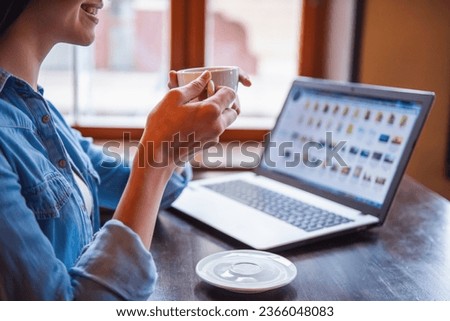 Cropped image of beautiful girl using a laptop, drinking coffee and smiling while sitting at the cafe
