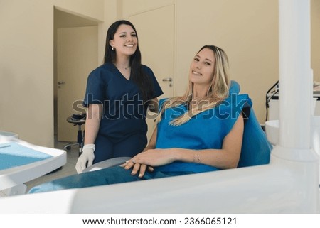 Young beautiful woman and female doctor at the dentist clinic looking at the camera and smiling