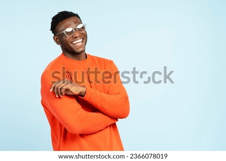Portrait of smiling attractive African American man wearing casual orange t shirt, stylish eyeglasses isolated on blue background. Concept of shopping, advertisement