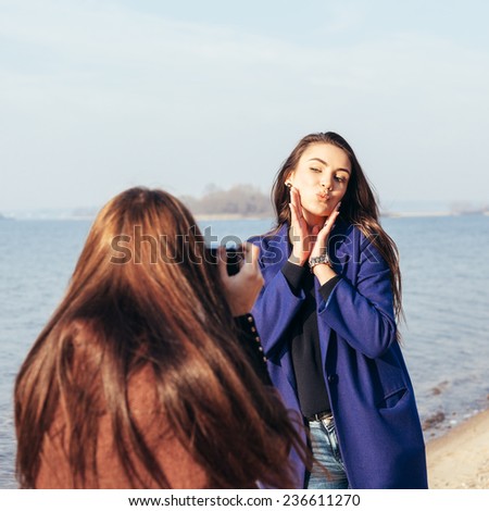 Cheerful young girl in a blue coat posing her girlfriend on the beach in front of the sea Outdoor lifestyle portrait