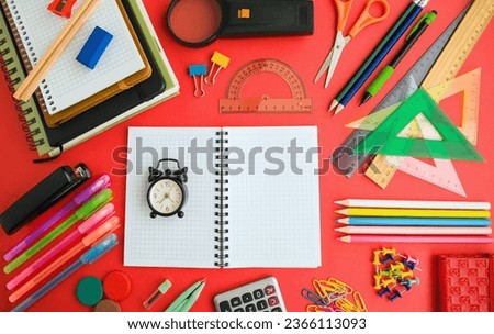 Colorful school supplies designed on red surface,with blank checkered notebook and mini vintage alarm clock,Conceptual image of education