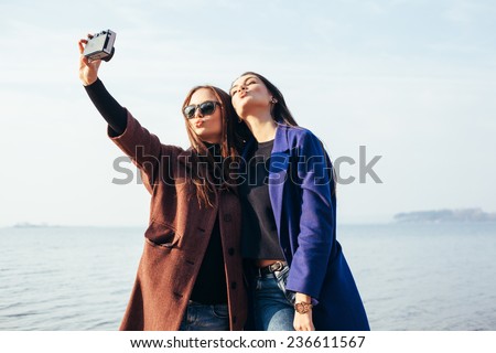 Two funny girlfriends doing selfie on the beach in front of the sea. Outdoor lifestyle portrait