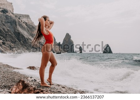 Woman summer travel sea. Happy tourist in red bikini enjoy taking picture outdoors for memories. Woman traveler posing on beach at sea surrounded by volcanic mountains, sharing travel adventure joy