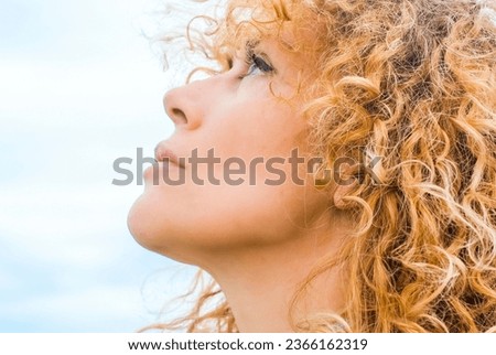 Close up of beautiful middle age woman face looking up in the air. Blonde natural curly hair. Female beauty adult. One lady thinking to ideas. Blue background sky. People and expressions portrait.
