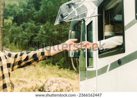 Concept of people travel together with love. One man and woman touching hands each other from inside a camper van to outside. Green nature forest in background. Traveler and destination. Vanlife