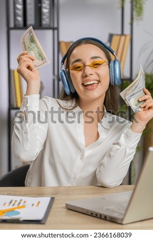 Business woman holding fan of cash money dollar banknotes celebrate, dance, success career, lottery jackpot game winner, big income, wealth at office workplace desk. Remote distant working. Vertical