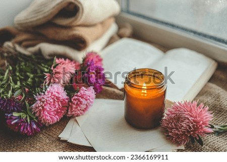 Burning candle, flowers, open book, cozy autumn.