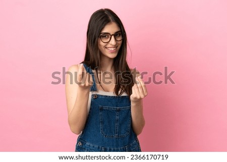 Young caucasian woman isolated on pink background making money gesture
