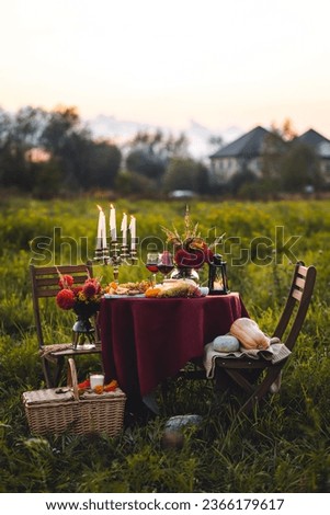 Elegant beautiful dinner table setting for thanksgiving or wedding celebration outdoors, fall countryside style, pumpkin as decor. Romantic atmosphere of a date, sunset. Cheese board, red wine