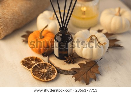 Autumn home perfume in glass bottle with wooden sticks, scented candles as apartment air freshener. Pumpkins, spices, cinnamon, anise. Aromatherapy, cozy atmosphere, comfort and relaxation