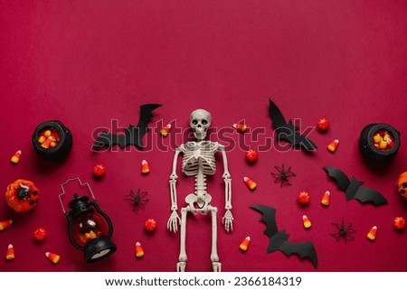Composition with tasty candy corns, skeleton, lantern and Halloween decor on red background