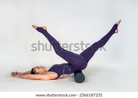 photo shows a charming cute young woman wearing a tracksuit stretching her back with a massage roller under her back. isolated on white background