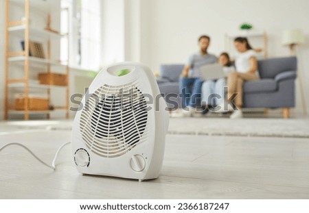 Close up shot of portable heater on floor at home. Closeup of white electric fan heater on floor in living room, with happy family on couch in background. Climate, temperature in the house concept Royalty-Free Stock Photo #2366187247
