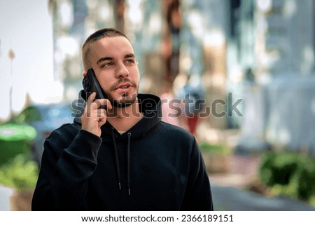 Cropped shot of a handsome young man using his cellphone while standing on the street in the city. Confident male wearing hoodie and having a call.