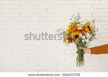 Female hand holding bouquet of beautiful autumn flowers on white brick background Royalty-Free Stock Photo #2366191703