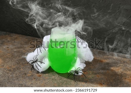 Spiders with glass of tasty cocktail for Halloween celebration on grunge table near black wall