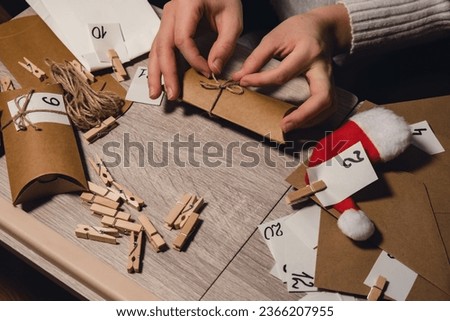 Unrecognizable young woman sticks number on craft bag, fastens with clothespin. Female making kraft paper for homemade advent calendar Made with your own hands step by step DIY crafts do it yourself
