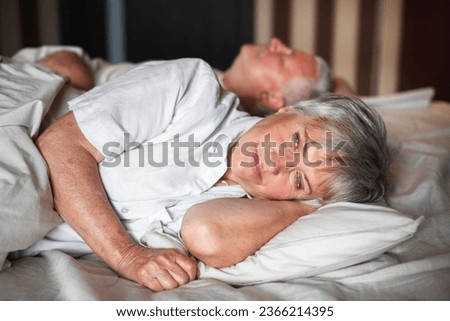 Refreshed elderly 60s woman wakes up in morning lying in bed in bedroom at home, middle-aged couple feels happy and peppy after enough sleeping, greeting new day, good morning concept Royalty-Free Stock Photo #2366214395