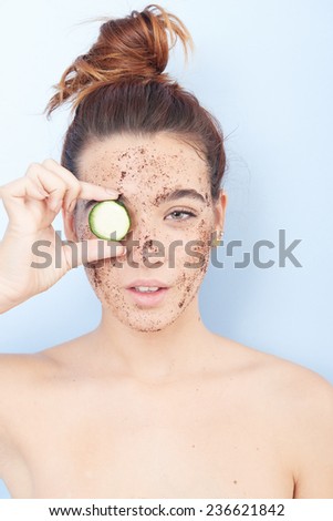 Woman with a facial scrub and biting a cucumber
