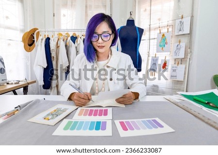 Fashionable freelance dressmaker is designing on new dress by drawing illustrator using color swatch while working in artistic workshop studio for fashion design and clothing business industry