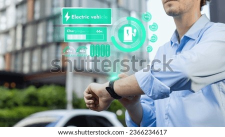 Businessman checking EV car battery status in hologram from smartwactch while recharging from charging station. Modern urban lifestyle and eco-friendly electric car utilization to reduce CO2. Peruse