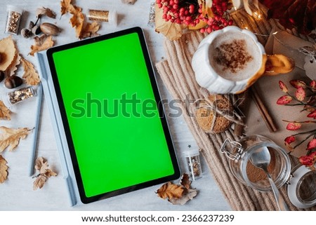 Tablet with green screen on the table. Workplace in autumn style concept. 